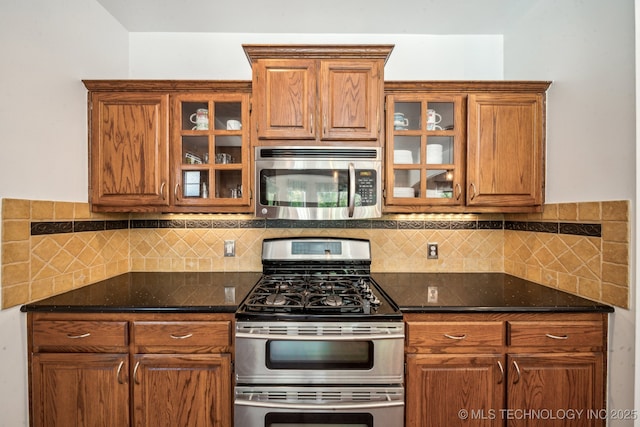 kitchen with appliances with stainless steel finishes, backsplash, glass insert cabinets, and brown cabinetry