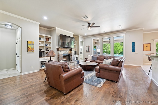 living room with ceiling fan, baseboards, a fireplace, light wood finished floors, and crown molding