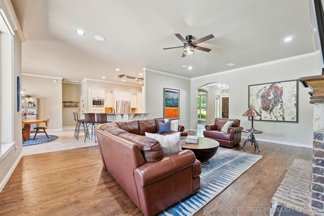 living area featuring arched walkways, ceiling fan, recessed lighting, ornamental molding, and light wood-style floors