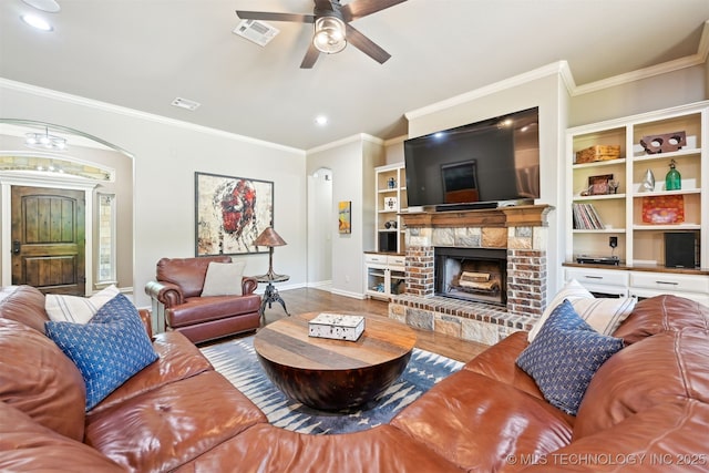living room featuring baseboards, arched walkways, a ceiling fan, a fireplace, and wood finished floors