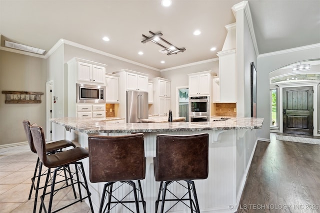 kitchen featuring appliances with stainless steel finishes, light stone counters, white cabinets, a peninsula, and crown molding