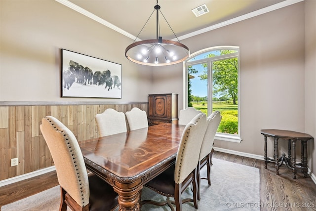 dining room with wood finished floors, crown molding, wood walls, a chandelier, and baseboards