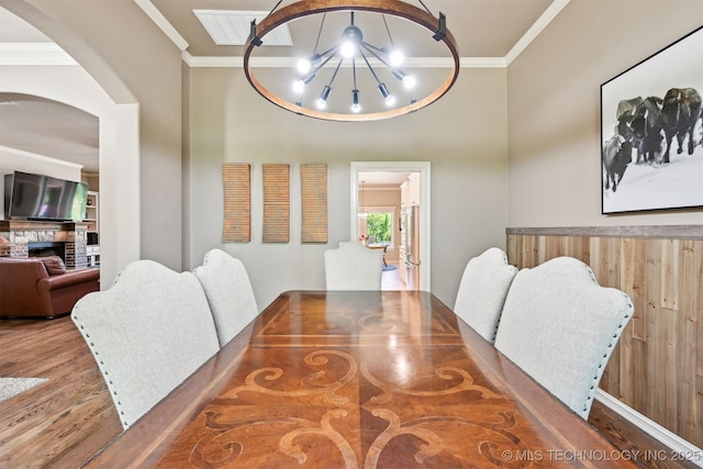 dining space featuring crown molding, wood finished floors, arched walkways, a chandelier, and a fireplace