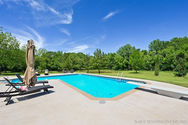 outdoor pool with a patio, a lawn, a diving board, and view of scattered trees