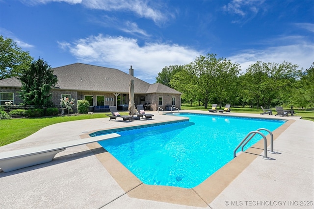 outdoor pool with a patio, a diving board, and a lawn