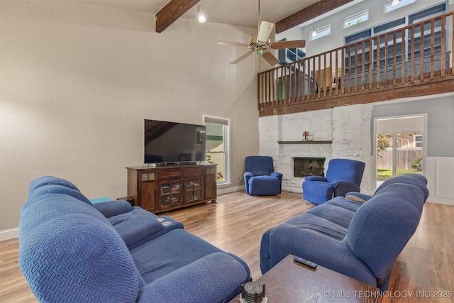 living area featuring beam ceiling, a towering ceiling, a ceiling fan, wood finished floors, and a stone fireplace