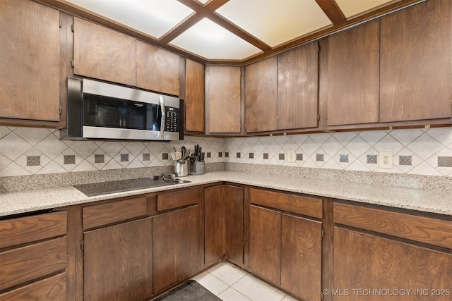 kitchen featuring stainless steel microwave, black electric stovetop, tasteful backsplash, and light tile patterned floors