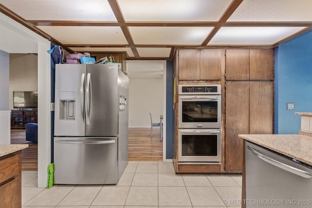 kitchen with stainless steel appliances, light countertops, light tile patterned flooring, coffered ceiling, and brown cabinetry
