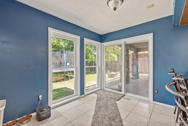 doorway to outside featuring light tile patterned floors, a textured ceiling, and baseboards