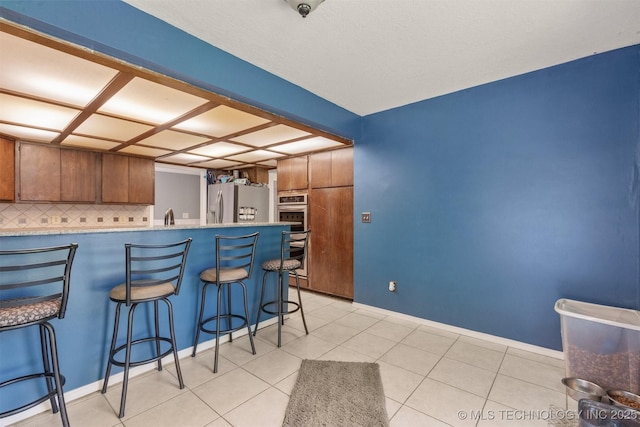 kitchen with appliances with stainless steel finishes, decorative backsplash, brown cabinetry, a kitchen breakfast bar, and a peninsula
