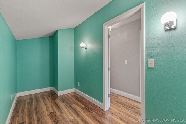 unfurnished room featuring wood finished floors, baseboards, and a textured wall