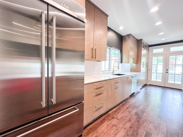 kitchen featuring stainless steel built in refrigerator, a sink, french doors, dishwashing machine, and wood finished floors