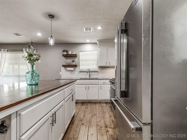 kitchen featuring stainless steel appliances, white cabinets, light wood finished floors, open shelves, and decorative light fixtures