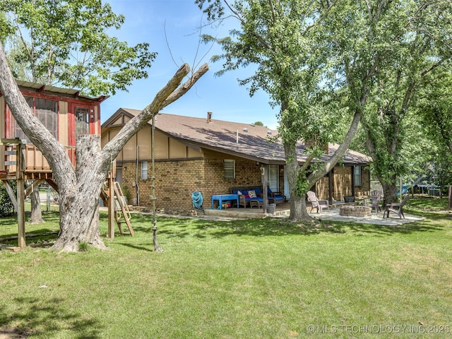 rear view of house featuring a fire pit, brick siding, a patio, a wooden deck, and a lawn