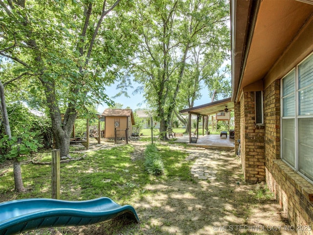 view of yard featuring a patio, ceiling fan, a playground, a shed, and an outbuilding