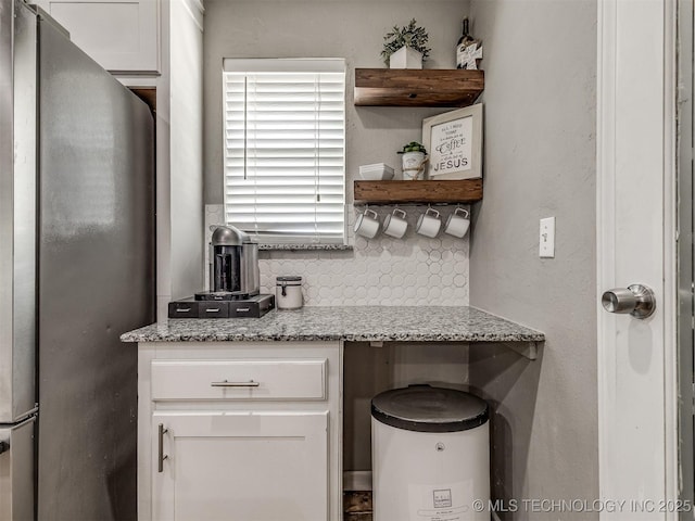 kitchen featuring freestanding refrigerator, open shelves, white cabinets, backsplash, and light stone counters