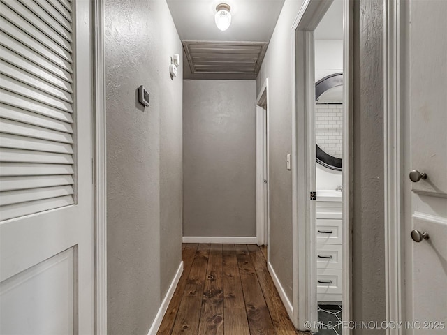 hallway with dark wood finished floors, a textured wall, and baseboards