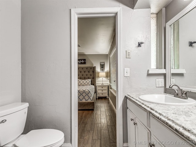 bathroom featuring toilet, ensuite bath, wood finished floors, vanity, and baseboards