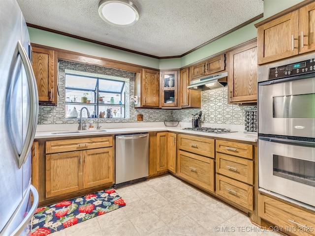 3931 S Oswego Ave, Tulsa, OK 74135 - kitchen featuring appliances with stainless steel finishes, a sink, under cabinet range hood, brown cabinetry, and a textured ceiling