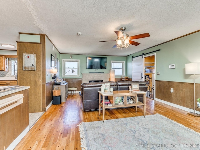 3931 S Oswego Ave, Tulsa, OK 74135 - living area featuring hardwood / wood-style floors, a ceiling fan, wainscoting, a textured ceiling, and a barn door