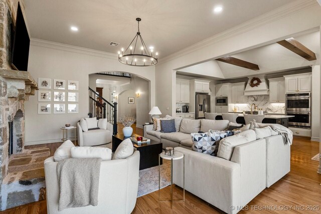 9475 E 107th Pl S, Bixby, OK 74133 - living room featuring arched walkways, a chandelier, crown molding, a stone fireplace, and light wood-style floors