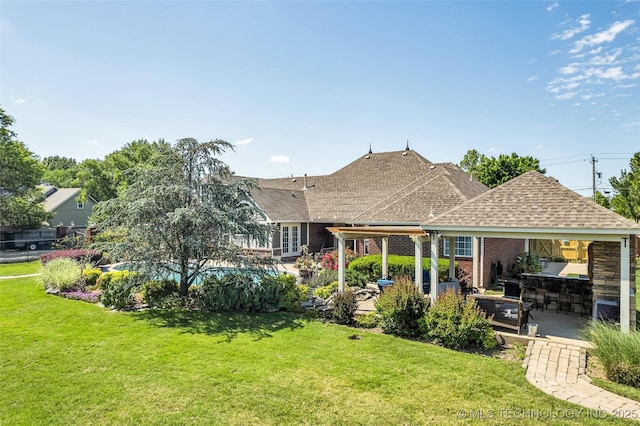 back of house featuring a shingled roof, a yard, a patio area, and brick siding