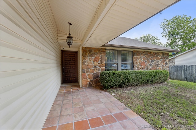 view of exterior entry featuring stone siding and fence