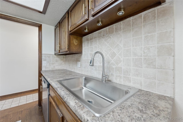 kitchen with a sink, light countertops, stainless steel dishwasher, tasteful backsplash, and a textured ceiling