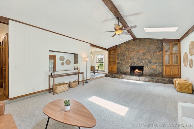 unfurnished living room featuring carpet floors, a ceiling fan, a skylight, a stone fireplace, and baseboards