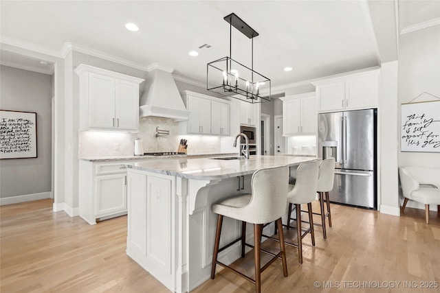 12113 S Fulton Ave E, Bixby, OK 74008 - kitchen featuring stainless steel appliances, premium range hood, light wood-type flooring, a spacious island, and white cabinets