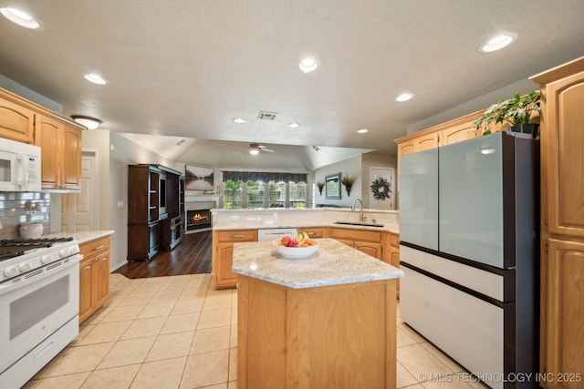 kitchen with white appliances, a sink, a peninsula, a lit fireplace, and light tile patterned flooring