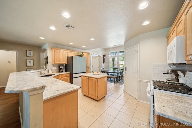 kitchen featuring arched walkways, white appliances, a sink, a peninsula, and light brown cabinets