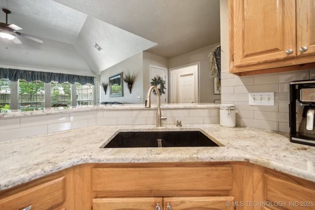 kitchen featuring a sink, decorative backsplash, ceiling fan, and light stone counters