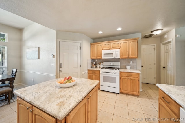 kitchen with white appliances, light tile patterned flooring, backsplash, a kitchen island, and light stone counters
