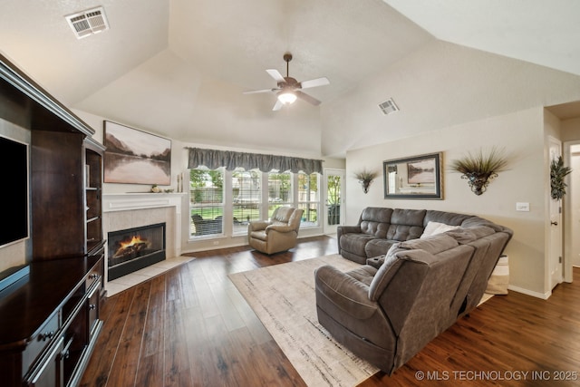 living room featuring lofted ceiling, ceiling fan, a tiled fireplace, and dark wood-style flooring