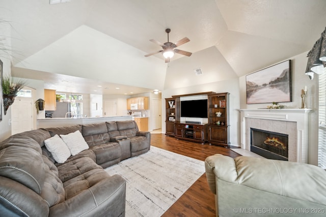 living room featuring a ceiling fan, wood finished floors, vaulted ceiling, and a tile fireplace