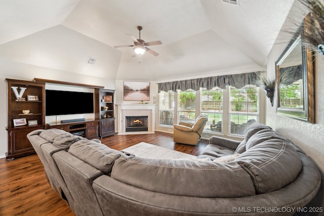 living area featuring vaulted ceiling, ceiling fan, dark wood-style flooring, and a fireplace with flush hearth