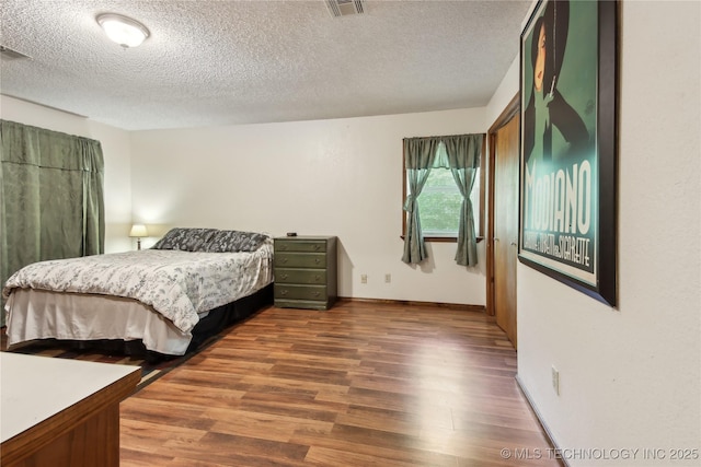 bedroom featuring wood finished floors, a textured ceiling, and baseboards