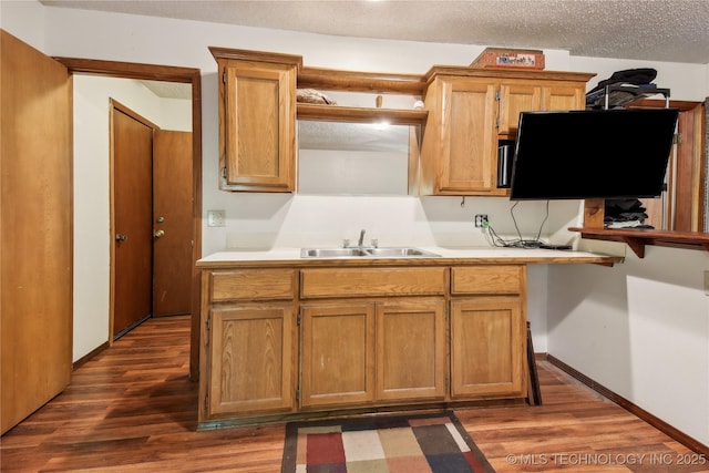 kitchen featuring a sink, dark wood-type flooring, light countertops, brown cabinets, and baseboards