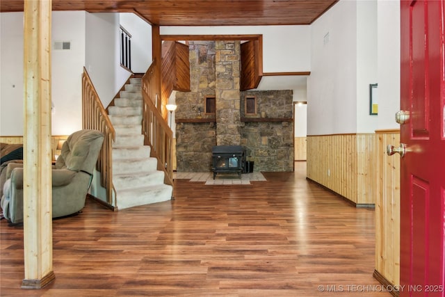living room featuring wood finished floors, a wood stove, stairs, a wainscoted wall, and wood ceiling