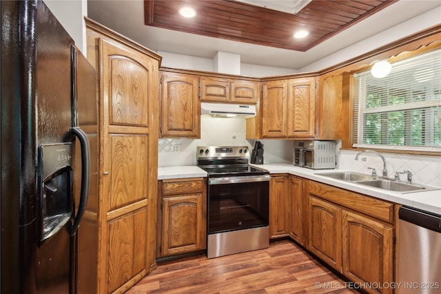 kitchen featuring stainless steel appliances, under cabinet range hood, a sink, light wood-type flooring, and backsplash
