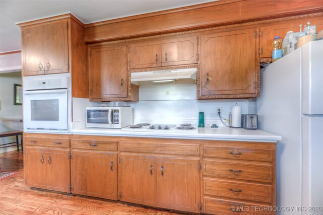 5102 S Columbia Ave, Tulsa, OK 74105 - kitchen featuring white appliances, under cabinet range hood, light countertops, brown cabinets, and light wood finished floors
