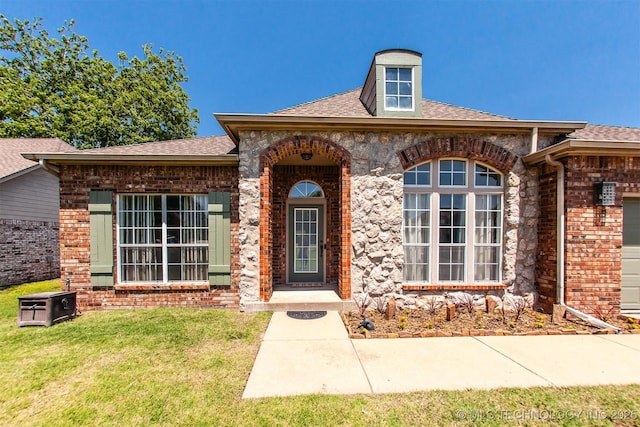 entrance to property featuring brick siding, a lawn, and a shingled roof