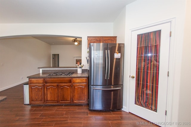 kitchen with freestanding refrigerator, arched walkways, dark countertops, and dark wood-style flooring