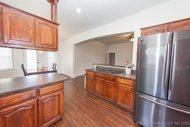kitchen featuring appliances with stainless steel finishes, arched walkways, dark countertops, dark wood-style floors, and recessed lighting