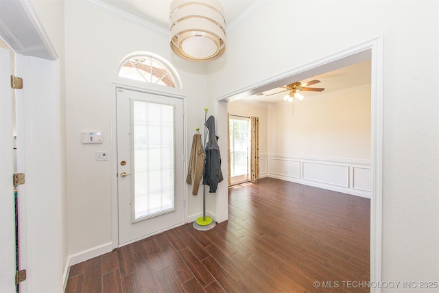 foyer featuring ornamental molding, healthy amount of natural light, dark wood finished floors, a ceiling fan, and a wainscoted wall