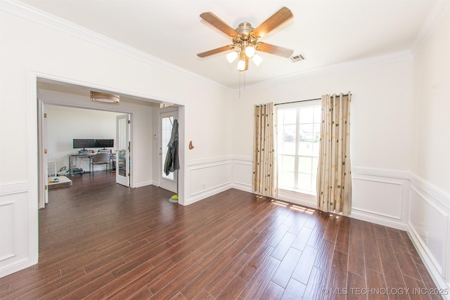 spare room featuring crown molding, dark wood-style floors, ceiling fan, wainscoting, and a decorative wall