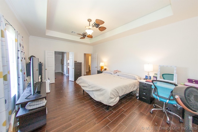 bedroom featuring a raised ceiling, dark wood-style floors, ceiling fan, and ornamental molding
