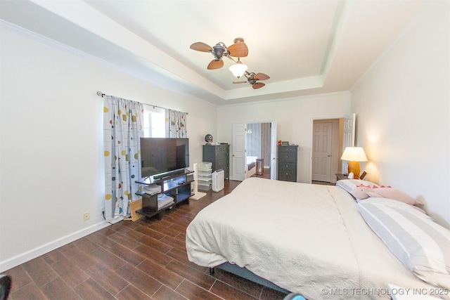 bedroom with a tray ceiling, dark wood finished floors, baseboards, and a ceiling fan