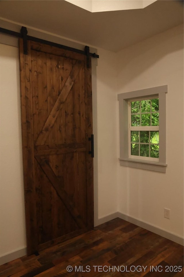 1185 E Pine St, Westville, OK 74965 - unfurnished bedroom with a barn door, dark wood-style flooring, and baseboards